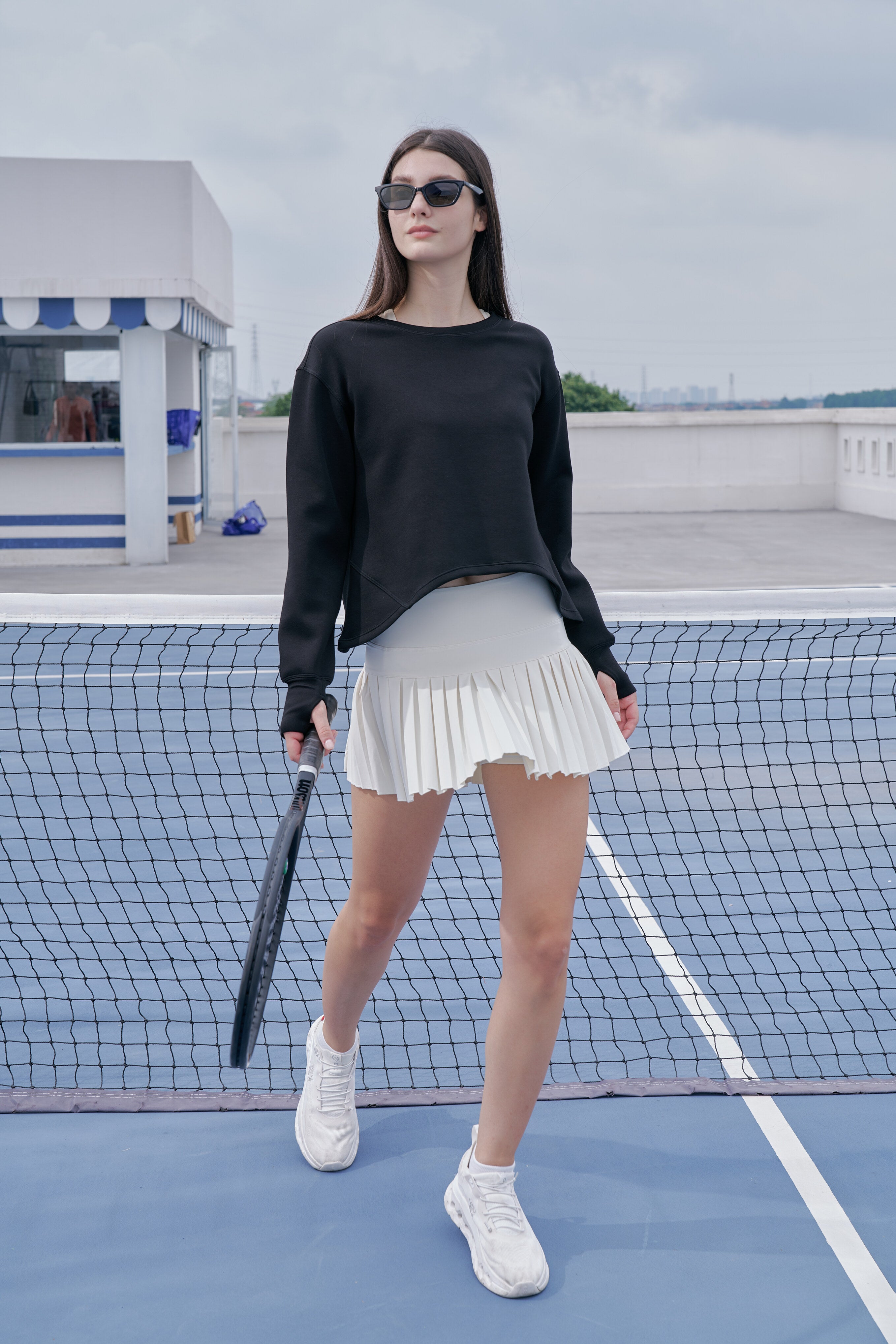 Woman on a tennis court wearing a black top and white skirt, holding a tennis racket.